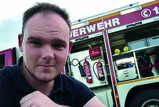 Stammzellspender Kevin aus dem Sauerland hockt vor einem Feuerwehrauto.