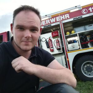 Stammzellspender Kevin aus dem Sauerland hockt vor einem Feuerwehrauto.