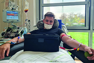 Ein junger Mann mit Mundschutz sitzt aufrecht in einem Entnahme-Bett und ist mit beiden Armen an ein Gerät angeschlossen.