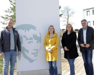 Vier Personen stehen vor einem Schild mit einer Illustration von Stefan-Morsch.