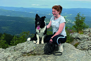 Eine Frau mit Pferdeschwanz sitzt mit einem schwarz-weißen Hund auf einem Felsen.