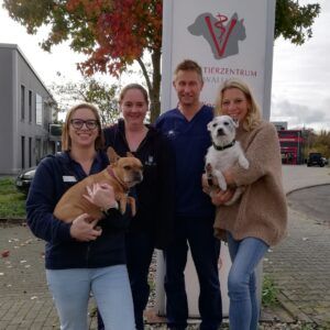 Carina Böcher und drei Arbeitskolleg:innen und zwei Hunde stehen vor dem Schild der AniCura Walluf GmbH